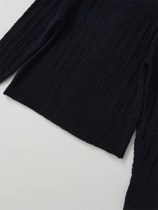 Détails du pull en maille sombre montrant la texture ajourée et les finitions de l'ourlet