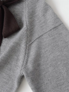 Close-up of fine grey knit texture and dark brown bow detail on fashionable hoodie