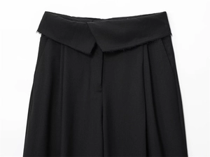 Dettaglio dei pantaloni neri a vita alta con bordo sfilacciato asimmetrico e pieghe