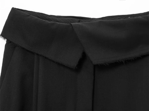 Dettaglio dei pantaloni neri in tessuto con vita asimmetrica e bordi sfrangiati
