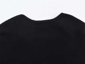 Detail of crew neckline on a black knitted poncho with high-density fabric texture