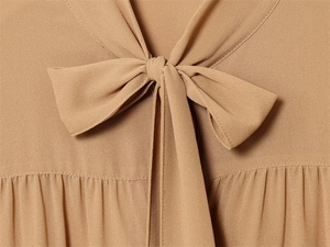 Dettaglio di una camicia in chiffon color cammello con elegante scollo a fiocco e pieghe