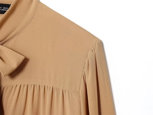 Dettagli di una camicetta in chiffon color cammello con elegante scollo a fiocco e ruches