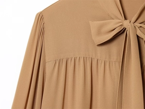 Dettaglio della camicia in chiffon color cammello con fiocco al collo e pieghe
