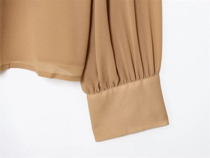 Dettaglio dei polsini pieghettati di una camicia in chiffon color cammello da donna