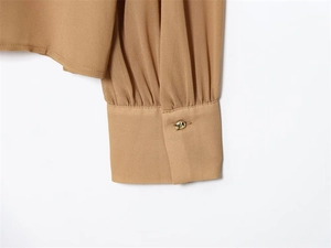 Dettaglio del polsino in chiffon color cammello con bottone dorato irregolare