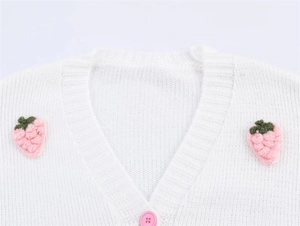 Detail der weißen Strickjacke mit niedlichen rosa Häkel-Erdbeeren am runden Halsausschnitt