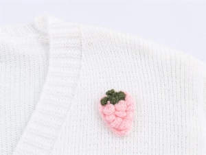 Nahaufnahme der handgestrickten rosa Erdbeere auf weißer Strickjacke mit Textur