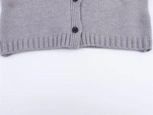 Detail of light gray knit cardigan featuring black matte buttons and ribbed hem texture