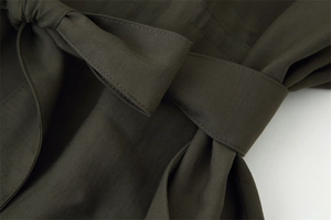 Macro detail of dark olive green coat featuring twill fabric texture and belt knot detail