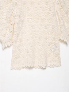 Detail eines cremefarbenen Strickpullovers mit feiner, wellenförmiger Lochstrickstruktur