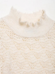 Detail eines cremeweißen Strickoberteils mit Lochmuster und Rüschen am Stehkragen