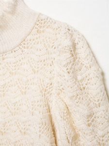 Detail eines cremefarbenen Häkelstrickpullovers mit Fransenhals und Spitzenmuster-Struktur