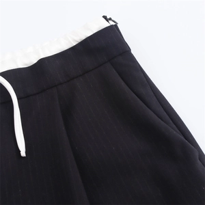 Dettaglio dei pantaloni neri gessati con coulisse bianca e cerniera laterale invisibile