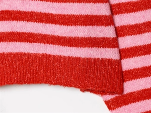 Gros plan sur la texture tricotée à rayures rouge et rose et l'ourlet côtelé