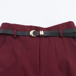 Dettaglio dei pantaloni bordeaux a vita alta con pieghe verticali e fibbia a mezzaluna d'oro