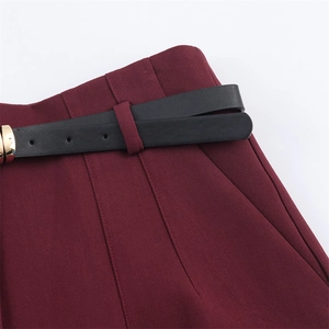 Dettaglio dei pantaloni rosso vino con sottile cintura in pelle nera e fibbia dorata