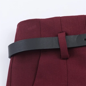 Dettaglio dei pantaloni rosso vino con vita alta e sottile cintura in pelle nera