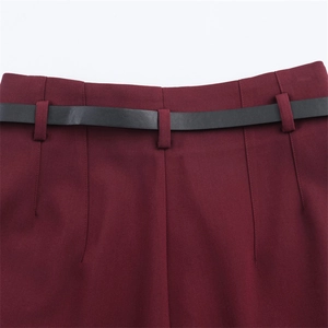 Dettaglio dei pantaloni bordeaux a vita alta con cintura nera sottile e trama del tessuto