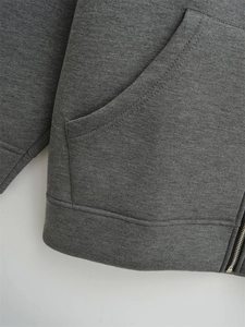 Detailed close-up of dark grey hoodie showing side pocket, metal zipper and ribbed hem
