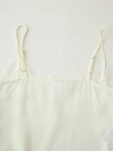Detail of white camisole top with adjustable straps and delicate lace trim on silk fabric