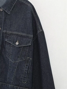 Dettaglio giacca di jeans blu scuro con cuciture a contrasto e bottoni in metallo