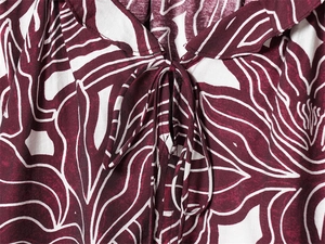 Close-up of ruffled collar with tie-up detail and tropical floral print on wine red fabric