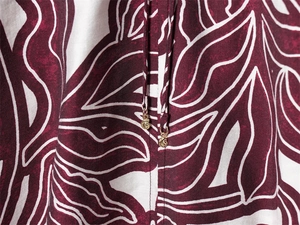 Close-up of burgundy leaf print on white textured fabric with golden spiral cord ends