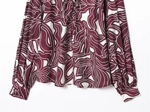 Detailed view of ruffle collar with tie and floral print on long-sleeved burgundy shirt