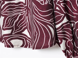Close-up of ruffles cuffs and vintage leaf print on smooth burgundy fabric blouse