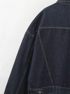 Dettaglio delle cuciture a contrasto e fibbia in metallo sulla giacca di jeans blu