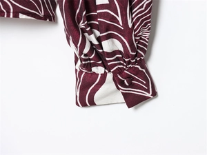 Detail of ruffled cuff with fabric-covered button on a burgundy leaf print long sleeve blouse