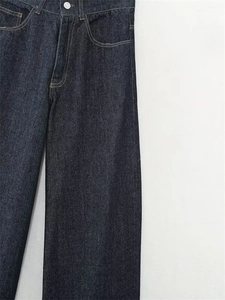 Dettaglio di jeans in denim indaco scuro con vita alta, bottone argento e cuciture