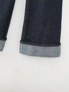 Dettaglio del risvolto sui jeans in denim blu scuro che mostra cuciture e trama del tessuto