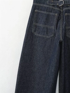 Dettaglio di jeans blu scuro a vita alta con ampie tasche e fibbie metalliche in argento