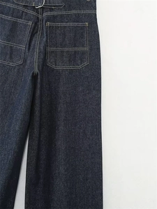 Dettaglio dei pantaloni in denim indaco con cuciture a contrasto e fibbie in metallo sul retro