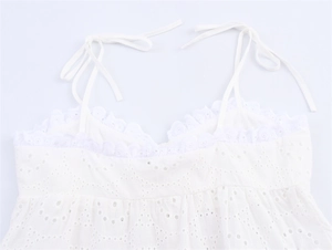 Detail van witte top met broderie anglaise, geschulpte kanten randen en strik schouderbandjes