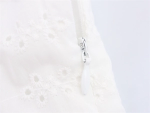 Detail van witte broderie anglaise stof met onzichtbare rits op een zomerse midi-jurk