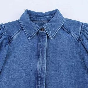 Détail des manches bouffantes et du col à revers sur une chemise en jean bleue