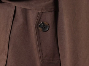 Detailopname van bruine trenchcoat met klepzak en knoop met marmeren textuur