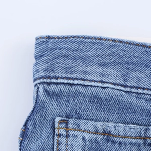 Macro du tissu denim bleu avec des surpiqûres contrastées précises sur le jean