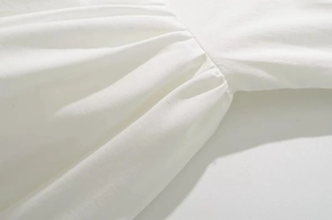 Detailed close-up showing the pleated fabric texture and neat stitching of white dress