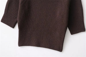 Detailed close-up of dark brown knit sweater with ribbed hem and sleeve cuff textures
