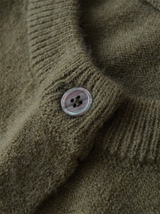 Détail d'un cardigan en grosse maille olive avec bouton marbré lilas et texture en laine