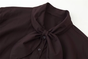 Detailed macro shot of the elegant pussy-bow neckline and buttons on the brown poplin shirt