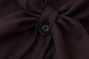 Detailed macro of a dark brown poplin shirt featuring a bow tie and black resin button