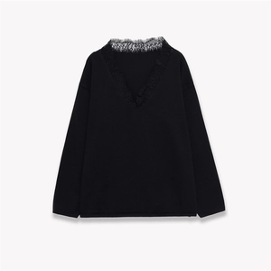 Detail of elegant black long-sleeve knit top featuring delicate lace trim on the V-neckline