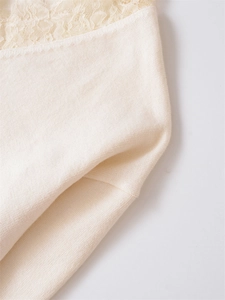 Close-up of cream knit fabric with delicate floral lace trim detail on the neckline