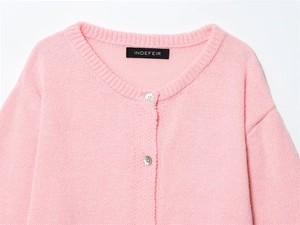 Dettaglio dello scollo del cardigan rosa con bottoni bianchi e trama morbida
