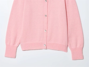 Dettaglio cardigan in maglia rosa con bottoni rotondi e polsini a coste su sfondo bianco